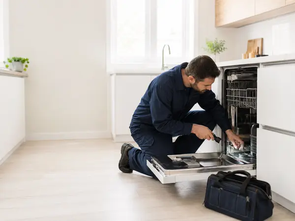 Appliance technician inspecting a dishwasher in a bright kitchen