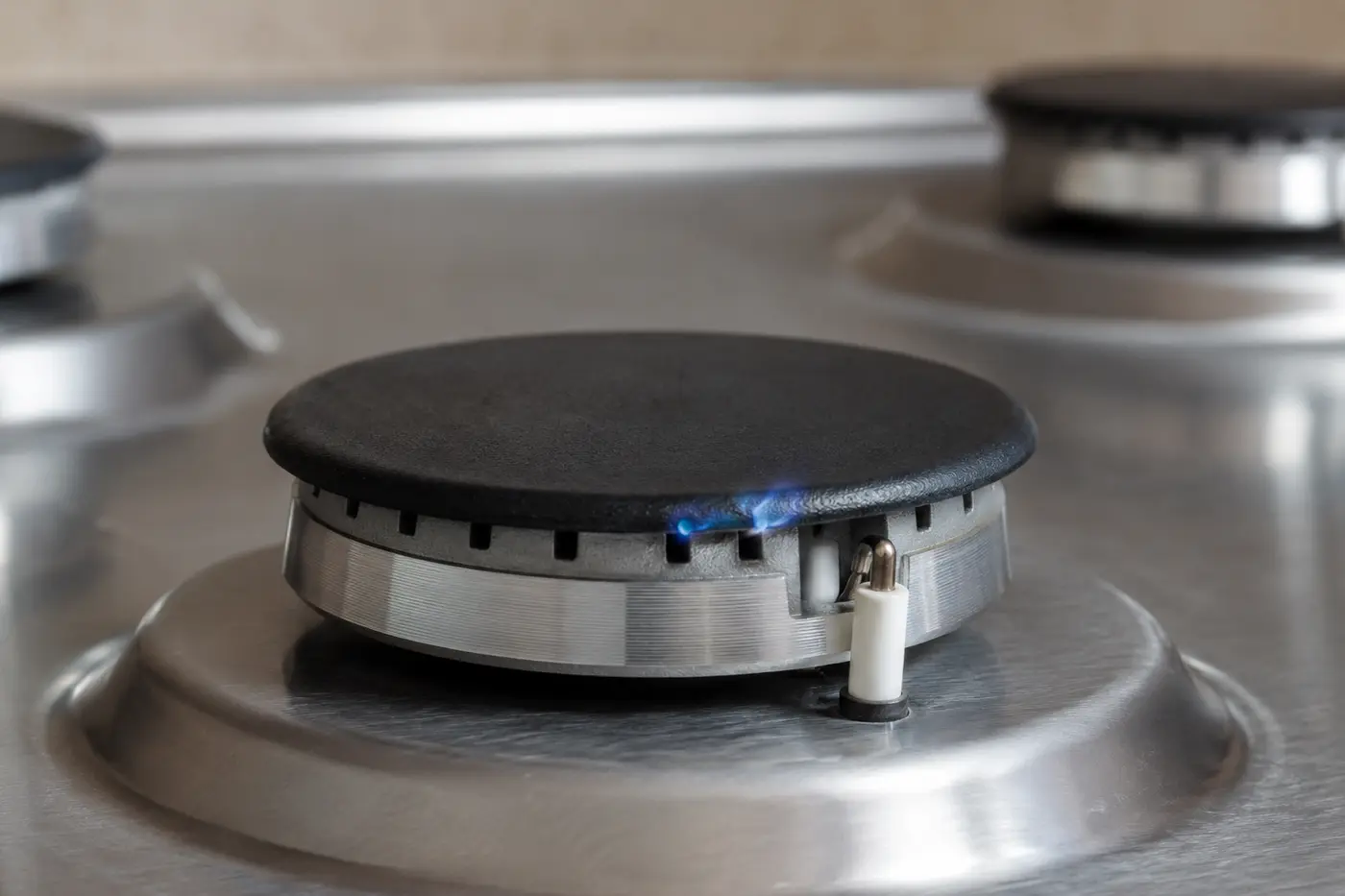 Gas cooktop burner with a small weak blue flame beside the ceramic igniter