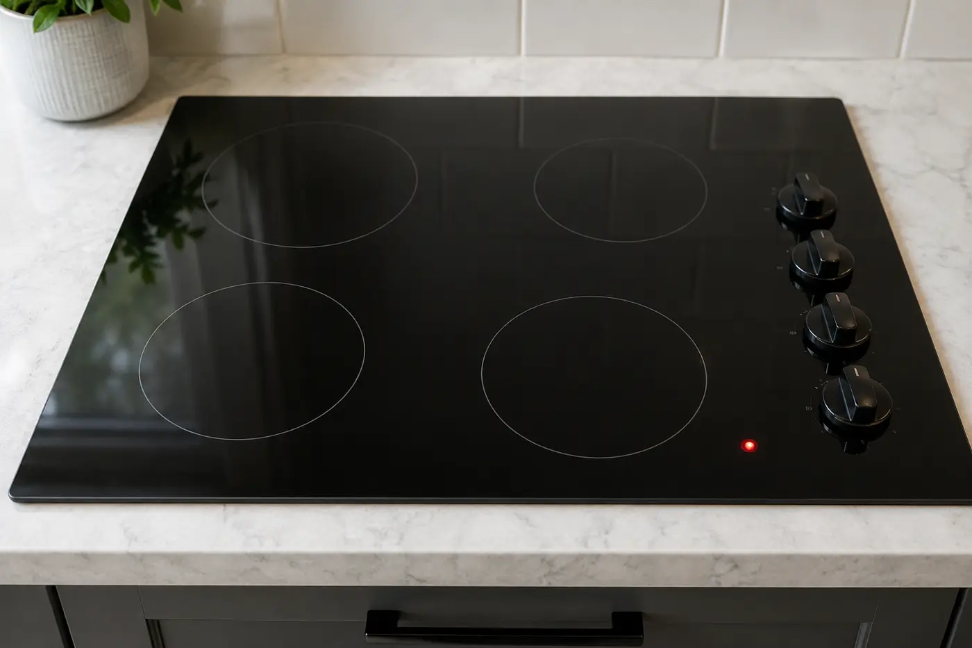 Powered-off glass cooktop with one red residual heat indicator still lit