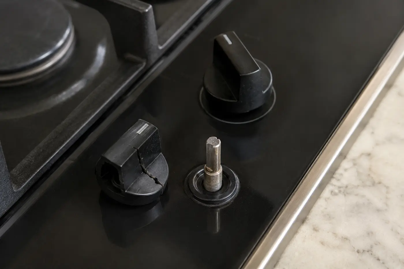 Cracked cooktop control knob beside its matching metal control shaft