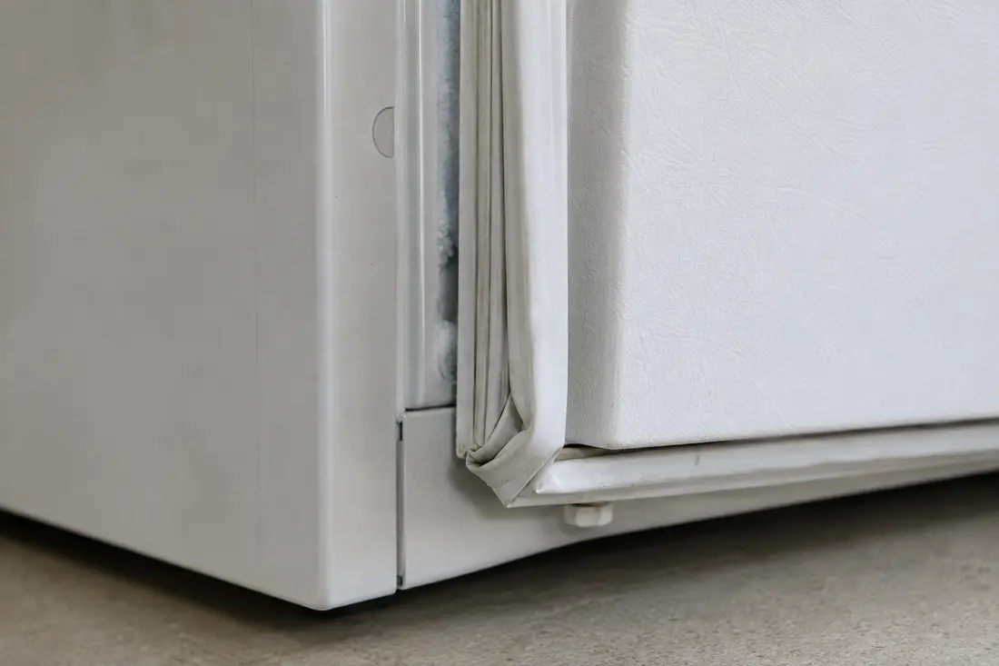 Flattened freezer door gasket creating a narrow gap at the lower corner