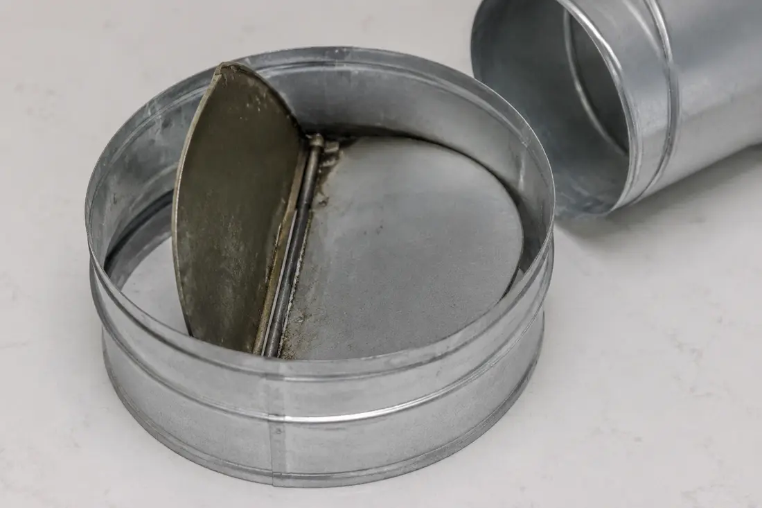 Round range hood exhaust collar with one backdraft damper flap partly stuck
