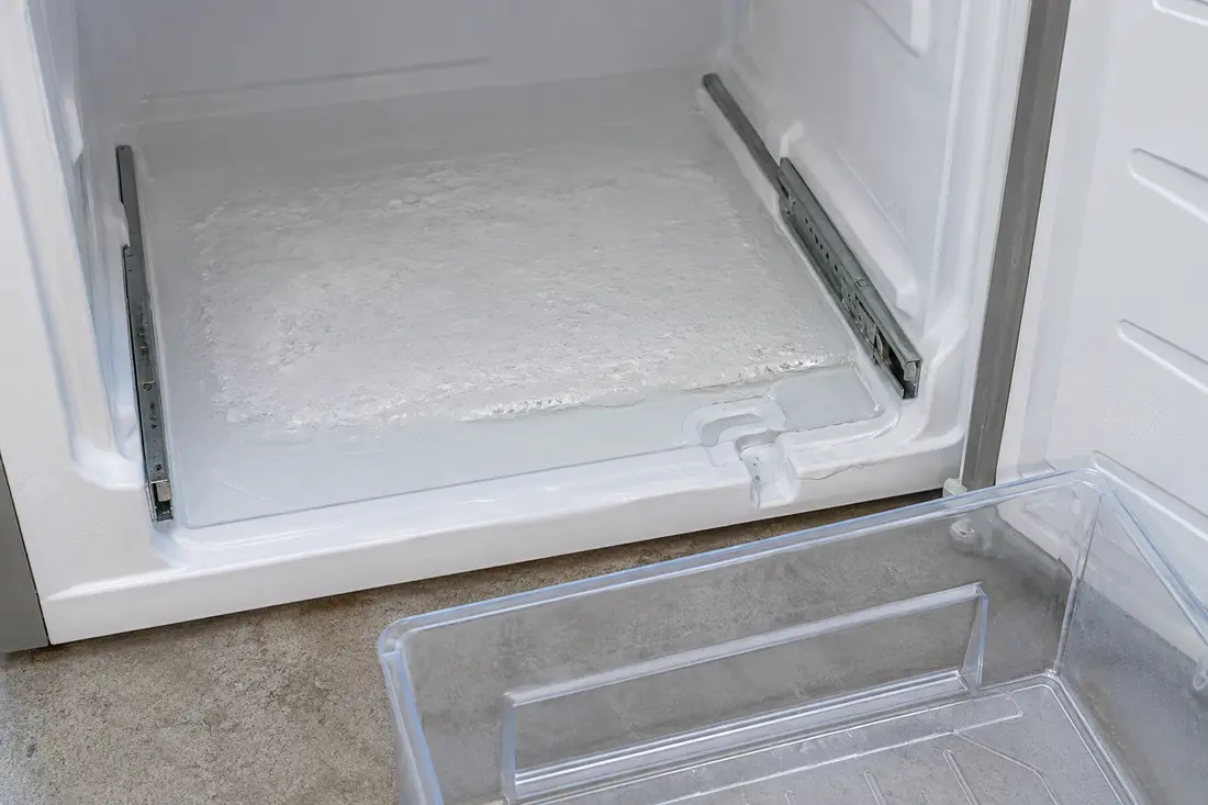 Frozen sheet of ice on the freezer floor beneath a removed drawer